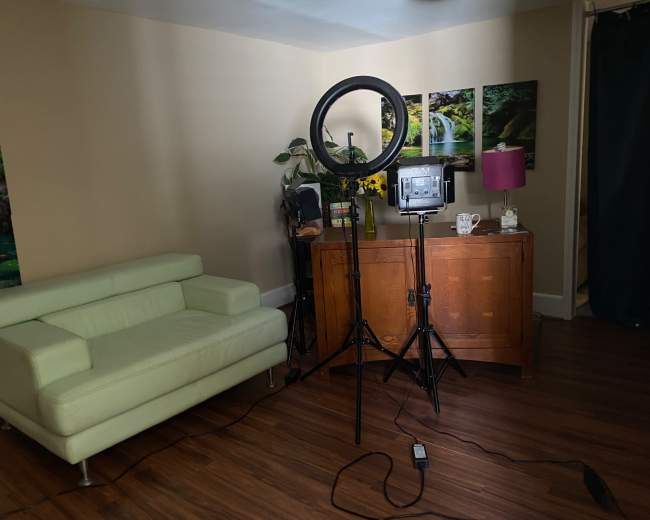 A well-lit room featuring a light ring on a stand, a wooden cabinet, a green couch, and decorative items on a surface.
