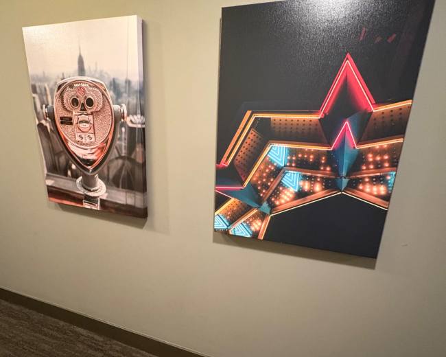 Two framed artworks hang on a wall; one depicts a viewfinder, and the other features a brightly lit star design.