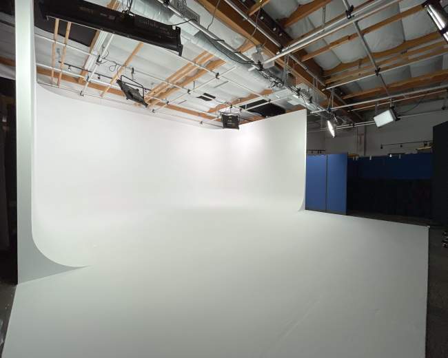 The image shows a spacious studio with a seamless white backdrop, overhead lighting, and a black section on the right.