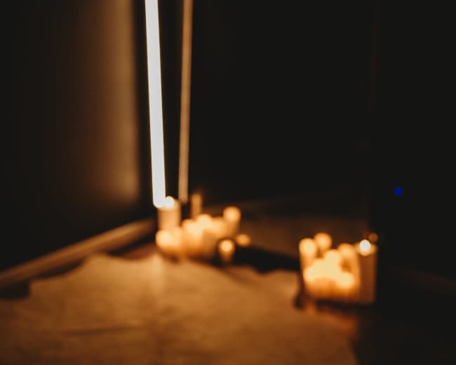 The image shows a dimly lit room with a mirror reflecting several candles arranged on the floor.