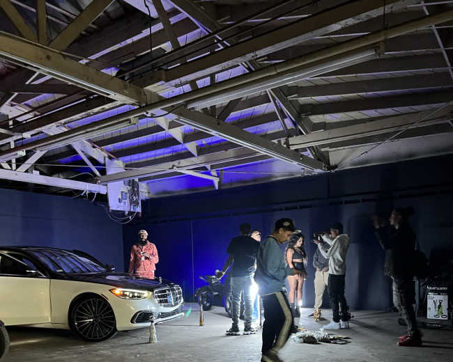A group of people gathers around a white car in a dimly lit garage space.
