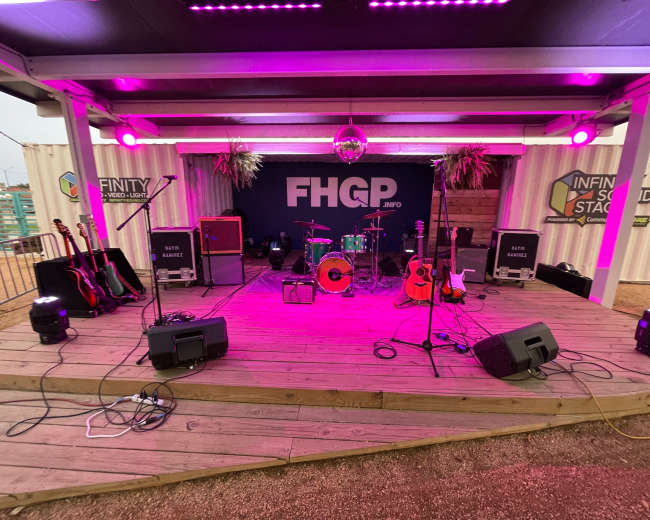 A stage setup features musical instruments, amplifiers, and a disco ball under purple lighting, ready for a performance.