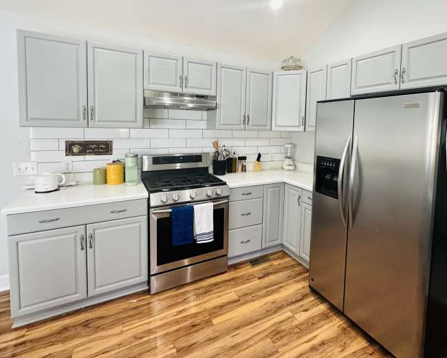 The kitchen features gray cabinets, stainless steel appliances, and a white tile backsplash, with wooden flooring.