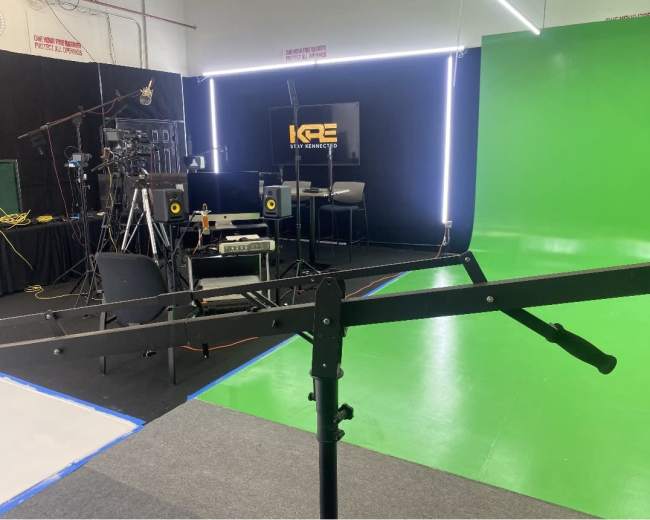 A studio setup featuring a green screen, cameras, lighting equipment, and a computer workstation.