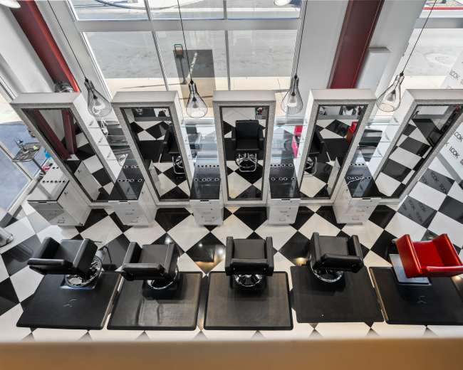 An aerial view of a barber shop with six black barber chairs arranged in front of mirrors on a checkered floor.
