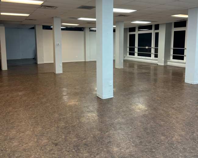 The image shows a spacious, empty room with a polished floor, featuring several columns and large windows.