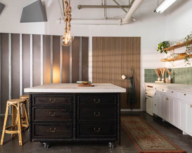 A modern kitchen features a central island with dark cabinets, a pendant light above, and white cabinetry against green tile.