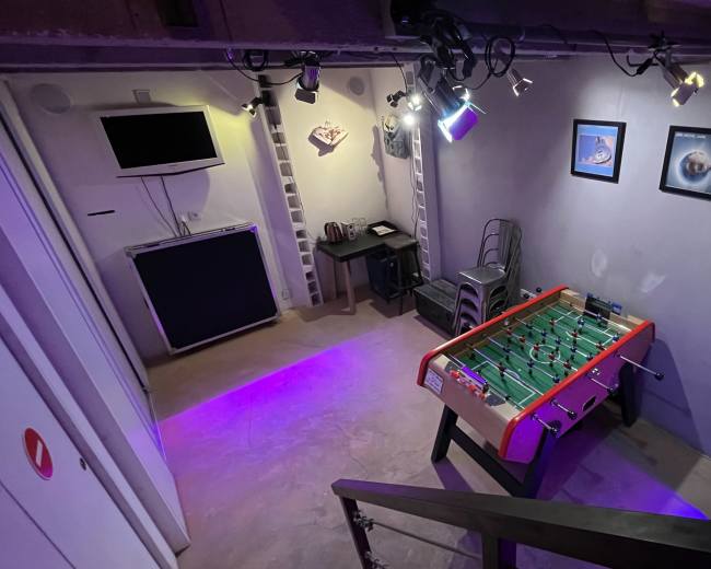 The image shows a basement game room featuring a foosball table, framed artwork on the walls, and ambient lighting.