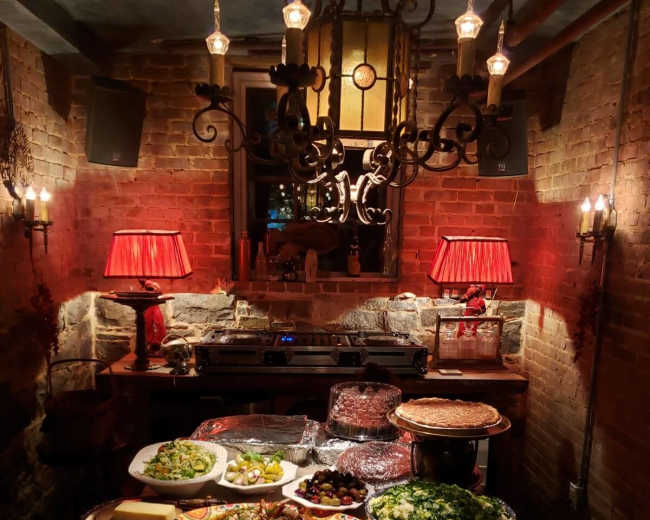 A table is set with a variety of dishes, including salads, pastries, and desserts, under warm lighting in a rustic room.