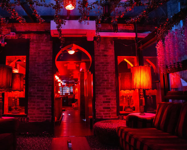 The interior of a dimly lit lounge features red lighting, decorative lamps, and brick walls.