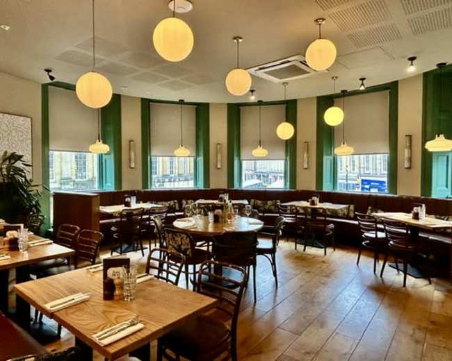 The image shows a modern restaurant with circular pendant lights, wooden tables, and green accent walls.