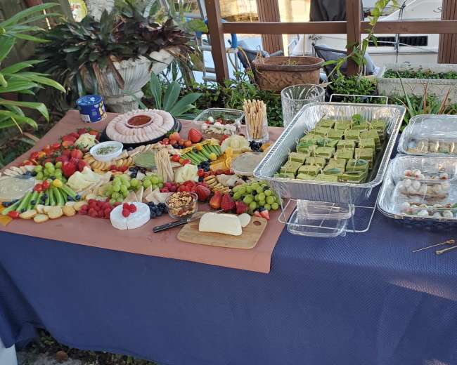 A buffet table is arranged with a variety of food, including fruits, vegetables, cheese, crackers, and desserts, set in an outdoor space.