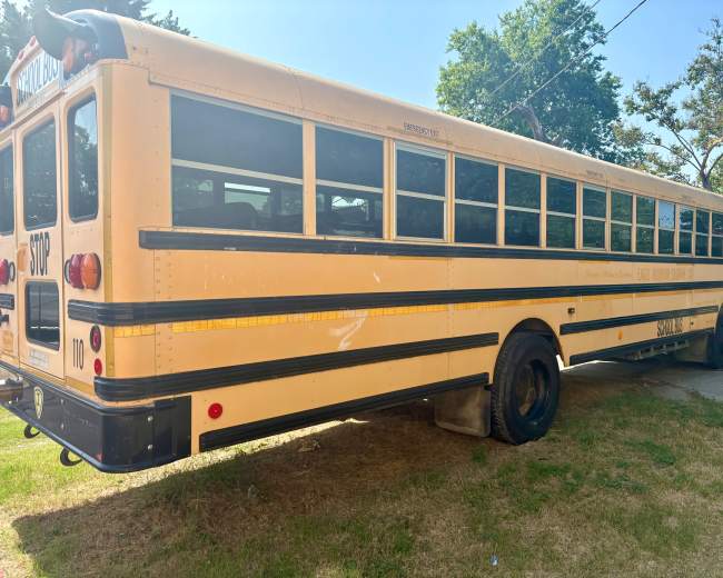 A yellow school bus is parked on a grassy area beside a road.
