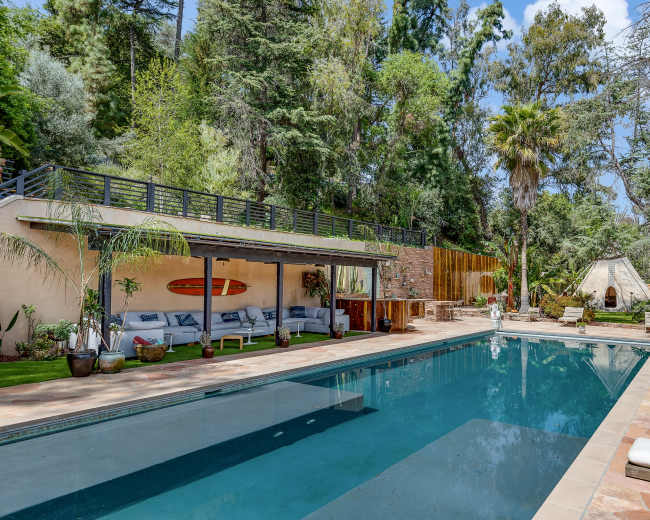 The image shows a swimming pool surrounded by loungers and a landscaped area featuring trees and plants.