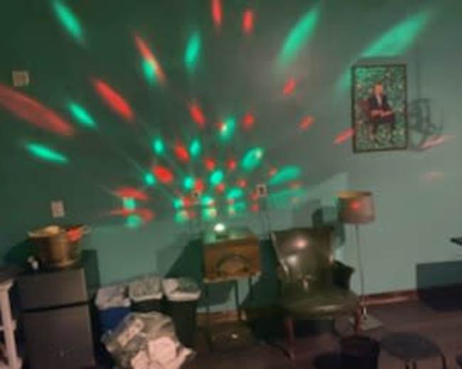 A room with a green wall, featuring chairs, a table, decorative lighting patterns on the wall, and a framed picture.