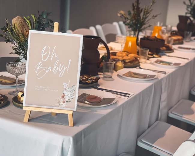 A long, elegantly set table with plates, drinks, and a decorative sign reading "Oh Baby! Welcome to Mali's Baby Shower."