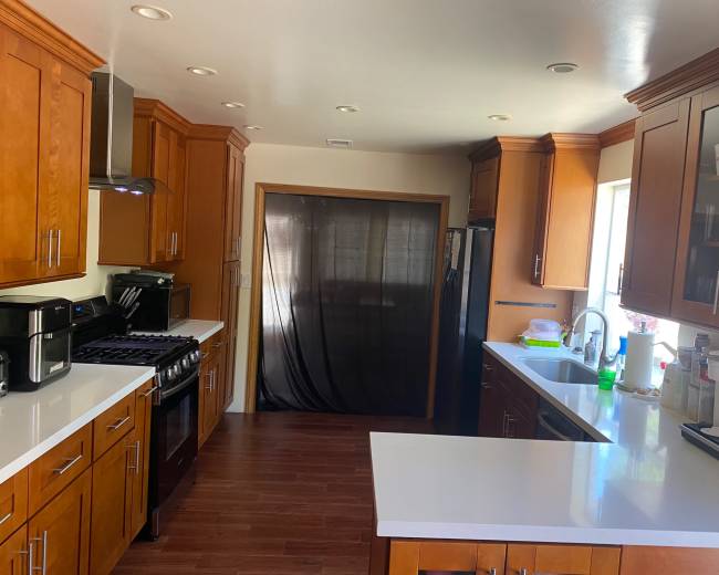 A modern kitchen features wooden cabinets, a gas stove, and a sink, with a partial view of a black curtain covering a doorway.