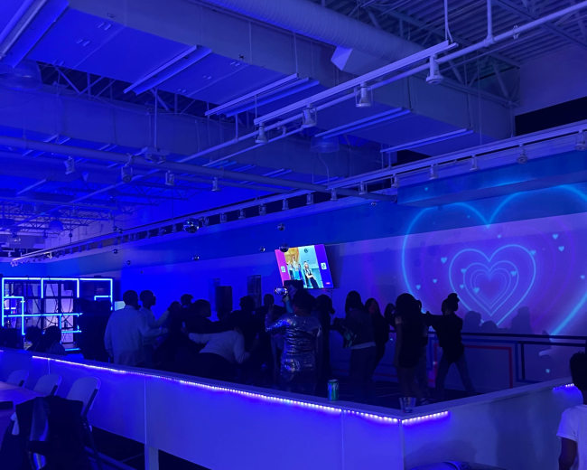 A crowd of people gathers in a dimly lit space illuminated by blue lights and multimedia screens.
