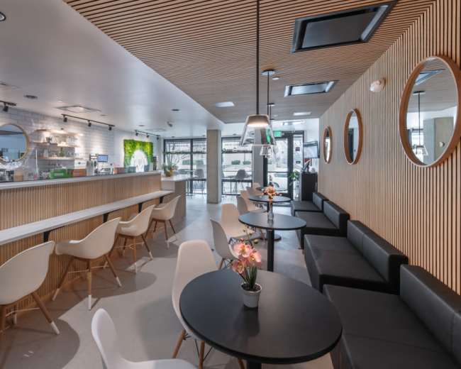 The image shows a modern café interior featuring wooden accents, circular mirrors, white chairs, and round black tables.