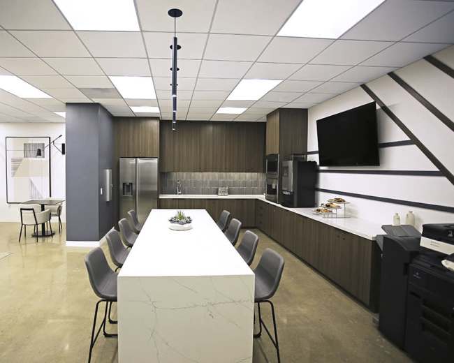 A modern kitchen and dining area featuring a large white countertop, bar seating for several people, and a well-equipped kitchen with dark wood cabinetry and stainless steel appliances.