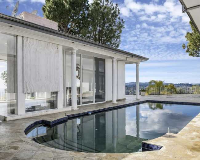 The image features a modern home with a pool, large glass windows, and columns overlooking a scenic landscape.