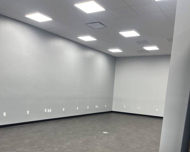 The image shows an empty room with gray walls, a gray floor, and fluorescent overhead lights.