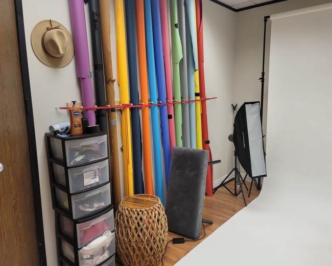 A photography studio with a backdrop of colorful rolls of paper, a storage unit, and lighting equipment.