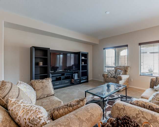 The living room features a large television unit, a glass coffee table, and upholstered seating arranged around the space.