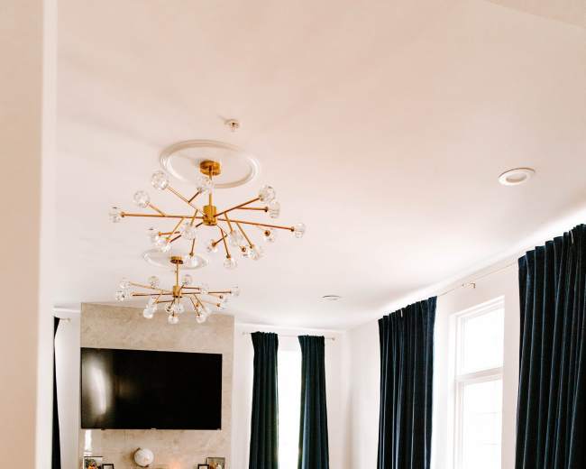 The living room features a fireplace with a TV above it, orange chairs, a zebra-patterned rug, and floor-to-ceiling dark curtains.