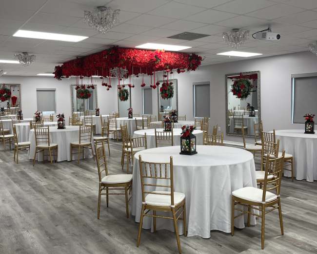 A decorated event space with round tables, gold chairs, and floral arrangements hanging from the ceiling.