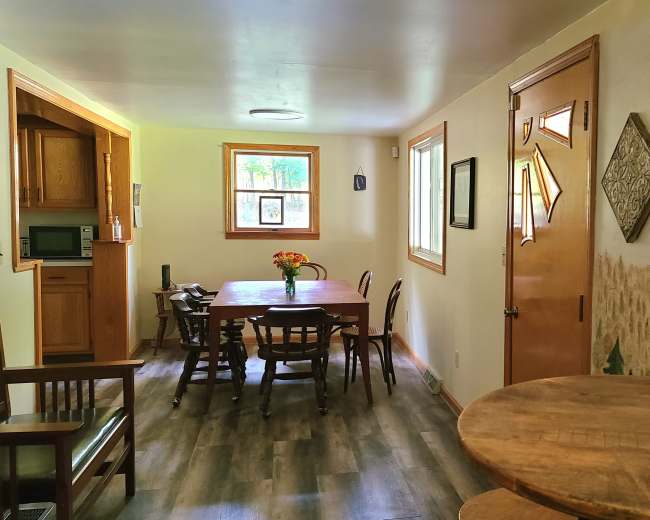 A bright room with a wooden dining table and chairs, a small kitchen area, and a door leading outside.