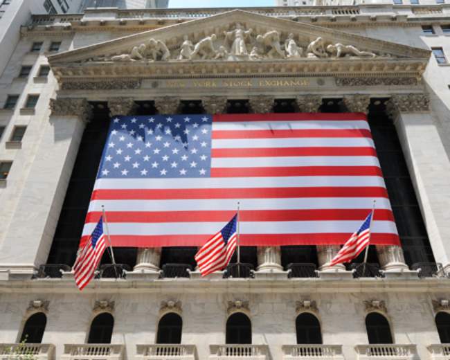 The New York Stock Exchange building displays a large American flag and features several smaller flags at its entrance.