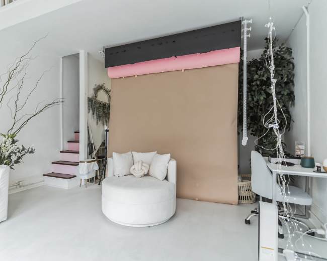 A spacious interior features a white couch, a circular chair, and a brown backdrop with a staircase and plants in the background.