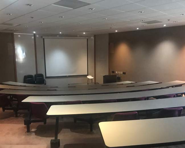 A lecture hall with tiered seating, a blank projection screen, and a small podium at the front.