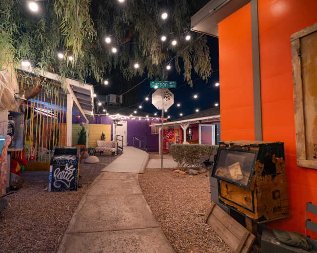 A vibrant pathway lined with colorful decor and string lights leads to a street sign at the intersection of Carson Street.