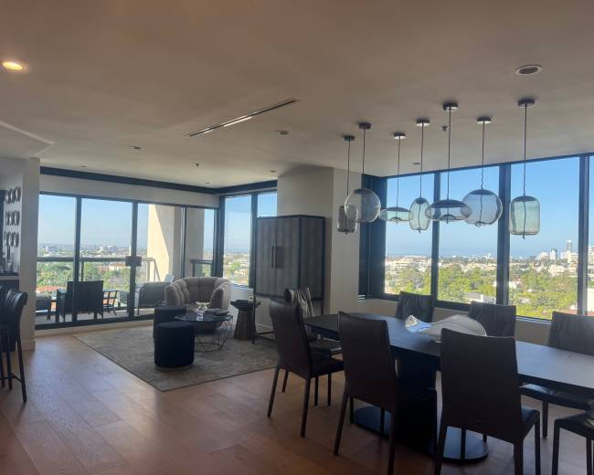 The image shows a modern interior of a stylish open-concept living and dining space with large windows offering a view of the city.