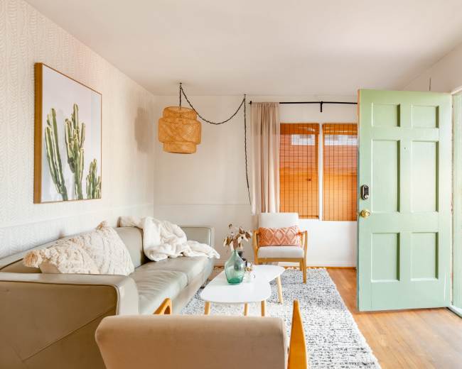A bright, inviting living room with a light green door open to an outdoor space, featuring a sofa, a small table, and a decorative light fixture.