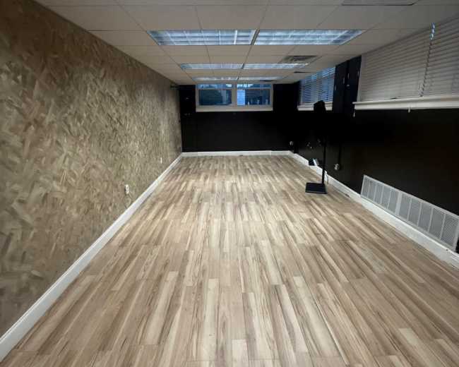 The image shows a spacious room with wooden flooring, a textured wall, and large skylights providing natural light.