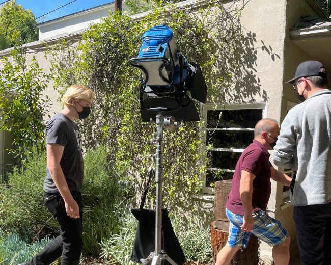 A portable floodlight is set up next to a pathway while two individuals walk in front of it.