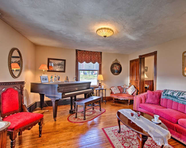 The living room features a grand piano, vintage furniture, and decorative mirrors, creating a cozy gathering space.