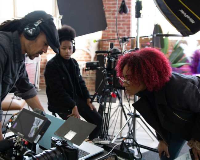 A group of filmmakers reviews footage on a laptop in a studio filled with cameras and lighting equipment.