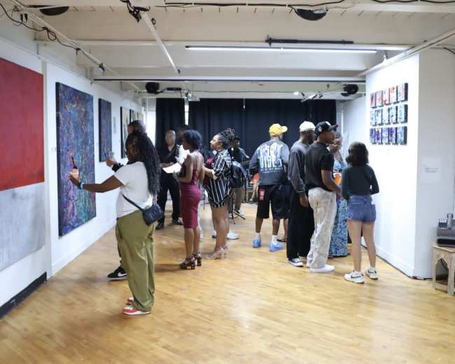 A diverse group of people explores an art gallery, examining colorful artworks on the walls.