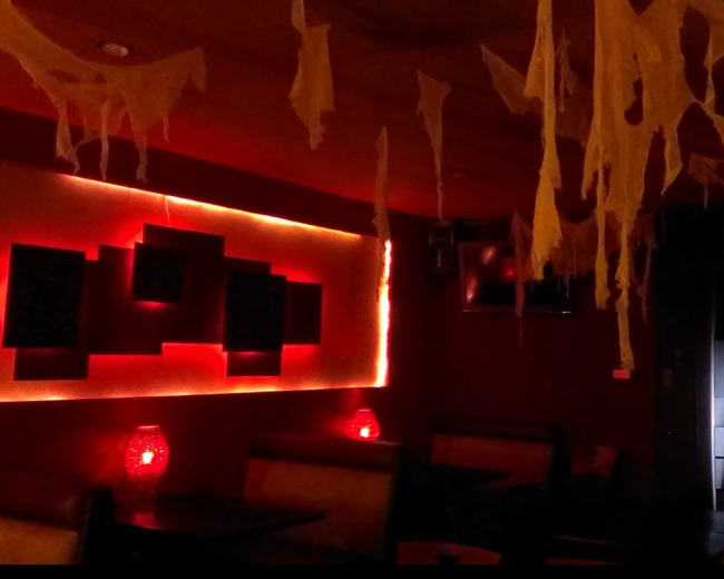 The interior of a dimly lit restaurant features cobweb-like decorations hanging from the ceiling, with red lighting illuminating the walls and tables.