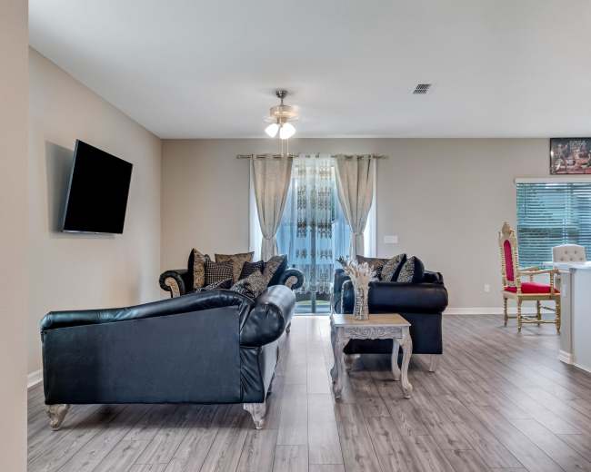 The living room features black leather sofas, a wooden coffee table, and a large window with sheer curtains.