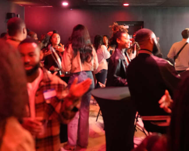 A group of people socialize in a dimly lit room with colorful lights.