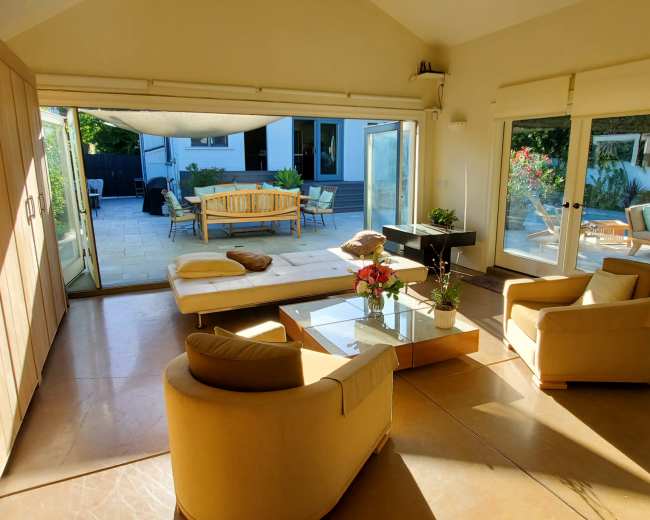 A sunlit room with a modern seating area, large windows opening to an outdoor patio with additional seating.