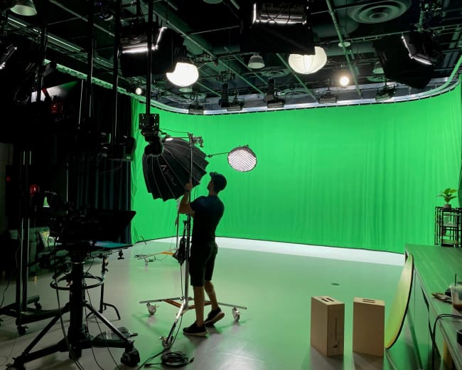 A person adjusts lighting equipment in a studio with a green backdrop.