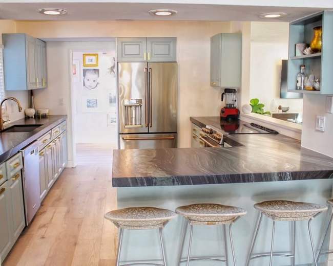A modern kitchen with light blue cabinets, stainless steel appliances, and a large island with four bar stools.
