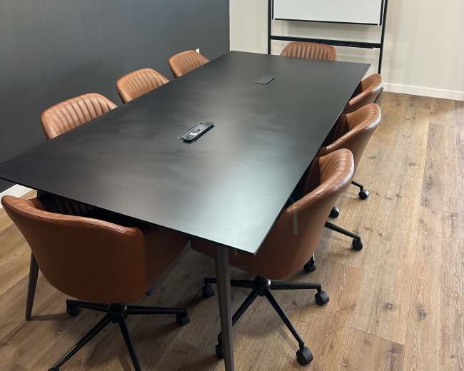 A modern conference room features a large black table surrounded by brown leather chairs, with a projector screen and minimalist lighting.