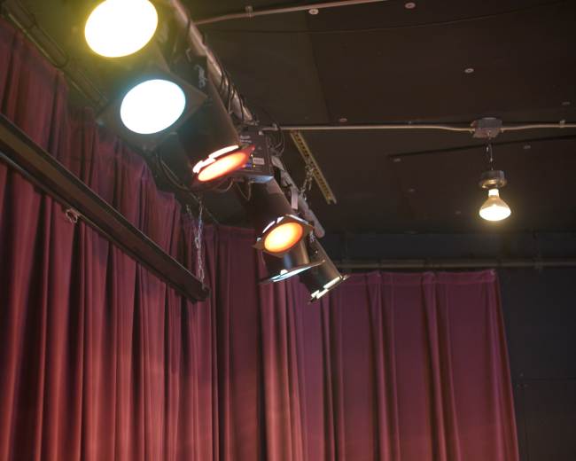 The image shows a stage setup with colored spotlights aimed at deep red curtains.